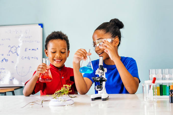 Two children examining colourful liquids beside a microscope