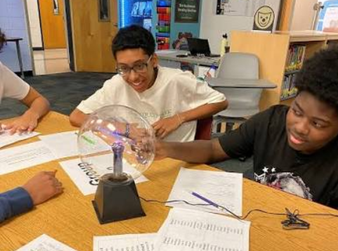 Young people laughing as they explore a plasma ball together during a hands-on science session
