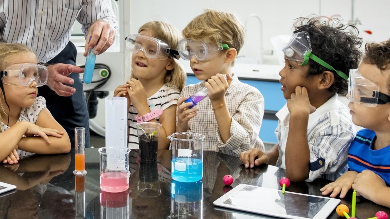 Children wearing safety goggles observing a teacher’s science demonstration