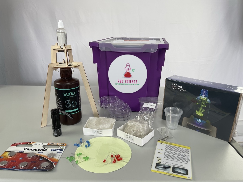 An ABC Science kit box with the charity logo, surrounded by lesson equipment: rocket launcher stand, LEDs, batteries, rocks and minerals